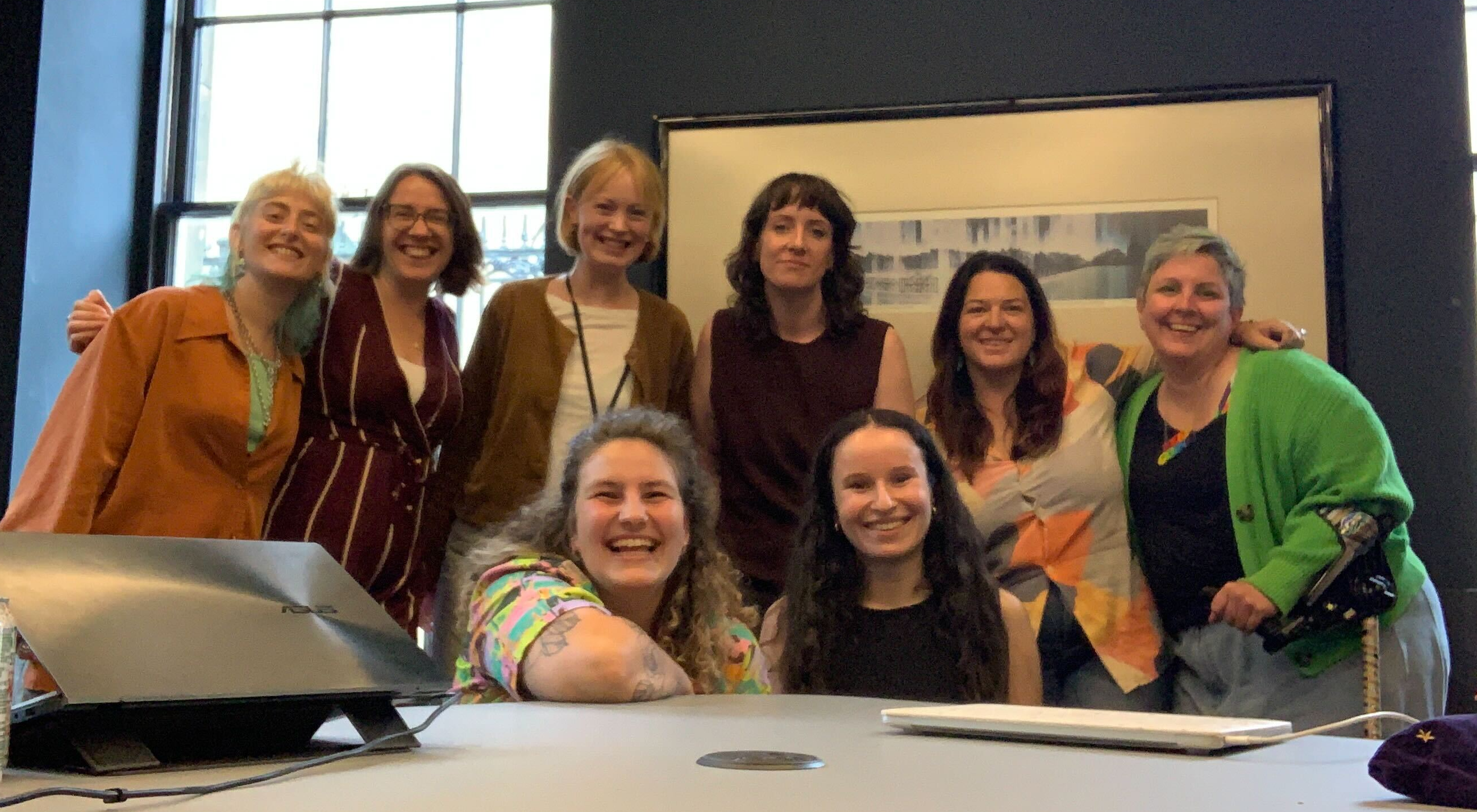 a team picture of 8 people smiling behind a table with laptops